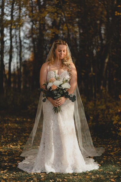 Bride stands in front of autumn colours holding bouquet