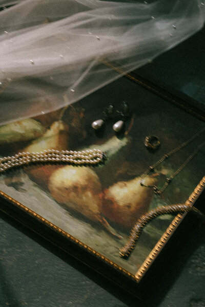 Rings, necklace, and bracelet flatlay on a painting with the bride's veil in Asheville, NC, photographed by Andrea-Marie Photography