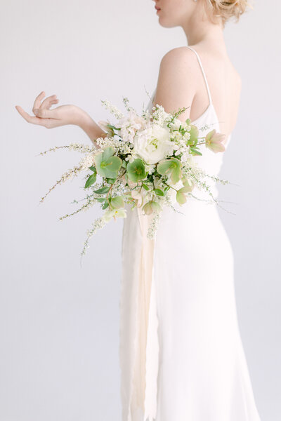 A bride in an elegant white dress holds an airy bouquet of white and green flowers.