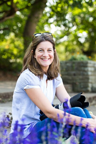 Portrait of Suzy Slemen smiling amid a blooming garden, showcasing the talented photographer behind the lens in her natural element.