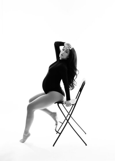 pregnant woman in simple bodysuit posing with chair in phoenix studio