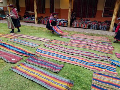 Indigenous women in traditional Andean dress arranging handwoven textiles on the grass at a weaving cooperative in the Sacred Valley ©Stephanie Dosch | theViatrix Peru Private Luxury Travel