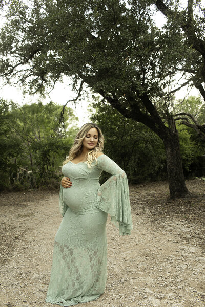 A peaceful maternity session with the expectant mother wearing a flowing green dress, her hands gently resting on her back and belly, capturing a moment of connection and serenity, photographed by Chunky Monkey Photography.