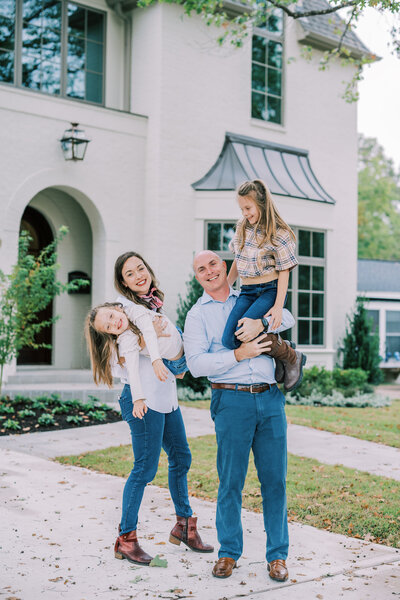 Mom and dad holding their two kids and smiling while standing in front of their house