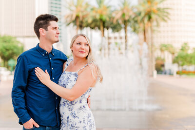 Bride shows off engagement ring while her fiance looks off camera in front of fountains in Downtown Tampa
