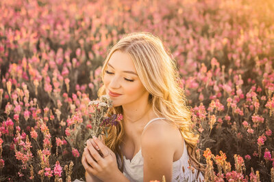 senior girl with long blonde hair looking down in a field of pink flowers
