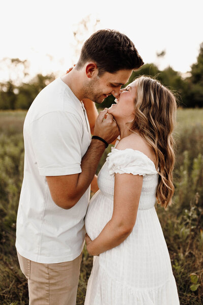 Couple leaning in to kiss while the woman holds her pregnant belly