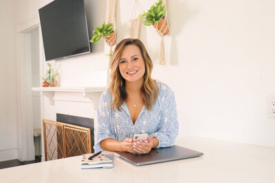 woman sitting at desk holding cell phone while smiling and wearing a blue shirt