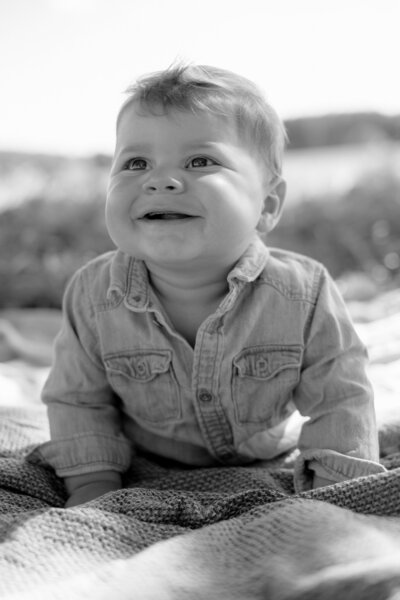 Ein kleiner Junge in Bauchlage blickt mit seinem zahnlosen Lächeln in die Ferne und stützt sich auf seine Hände.