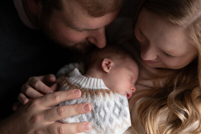 new mother and father snuggle in with newborn daughter as she lays on mother's chest