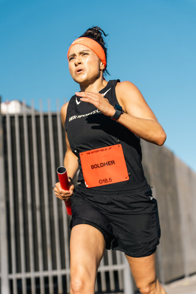 HER Sports Club member running outdoors with a relay baton.