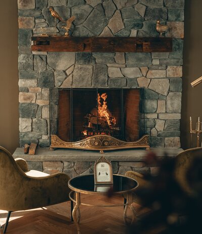 A warm fire burns in a stone fireplace is a rich, cozy room.