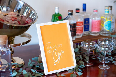 Orange wedding bar sign saying "Let the party Be-Gin" in white frame