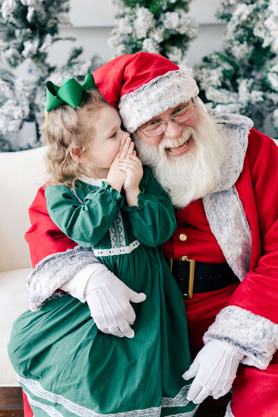 Santa huggin girl while she whispers in his ear