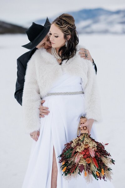Groom kisses bride's shoulder during winter elopement at  Lake Dillon.