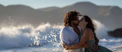 Couple kissing each other at the beach during sunset with large waves crashing in the background