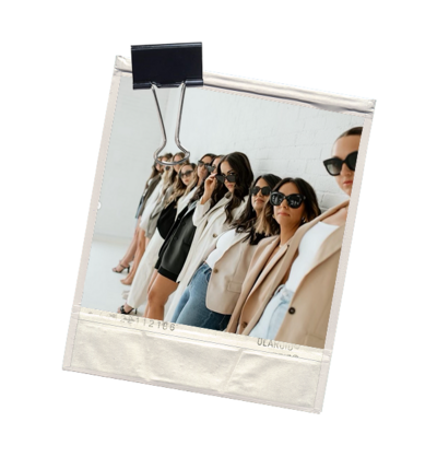 A line of woman leaning against a white brick wall that are all a part of a female community focused on health, wellness and professional careers. 