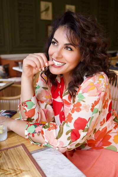 woman smiling at a desk with her thumbnail in her teeth