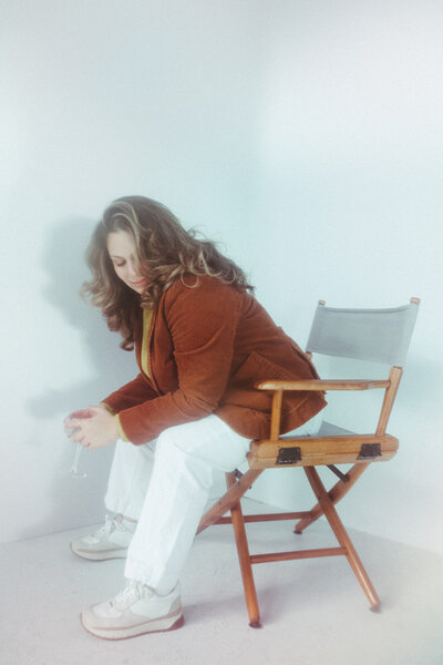 Sara Dobbins leans forward in chair and looks at the floor in a white corner