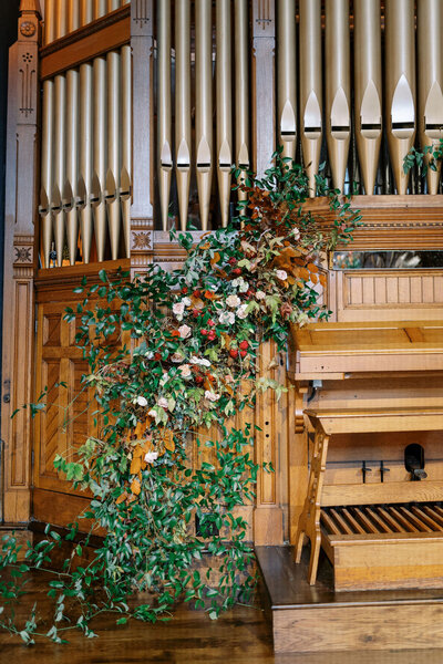 Lush and whimsical asymmetrical installation highlighting the organ was filled with greenery, autumnal foliage, and garden roses. Floral Design by Rosemary and Finch in Nashville, TN.