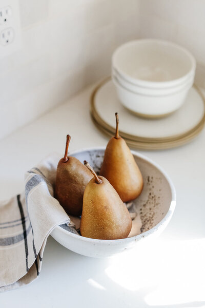 A bowl of pears styled on a white countertop.