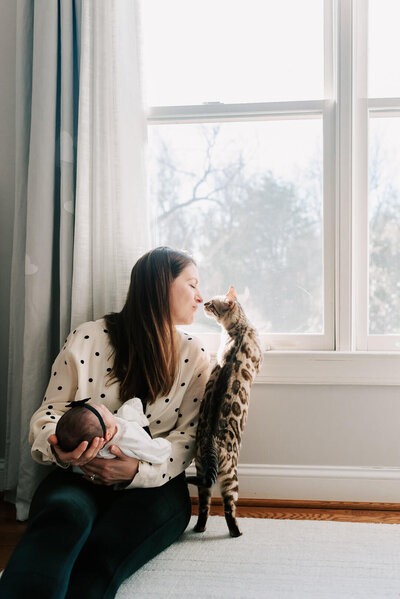 A mother holding her newborn daughter, enjoying a sweet moment with her snow bengal, taken by northern va newborn photographer