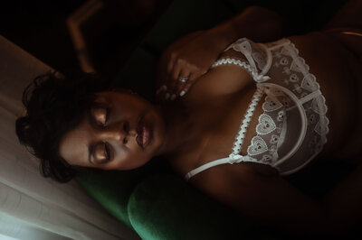 A woman wear a white lace embroidered bra while sitting on a couch under a window