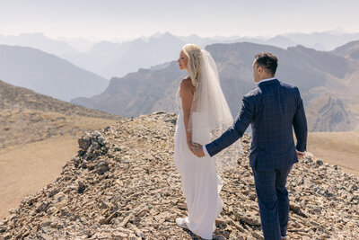 This truly epic photograph captures the bride and groom holding hands atop a mountain during their helicopter elopement. The stunning landscape and adventurous spirit of their wedding create an unforgettable and breathtaking moment, celebrating their love amidst nature's grandeur.