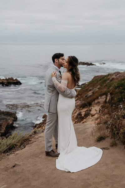 bride and groom standing on cliff overlooking the ocean in California