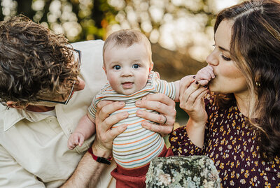 mom and dad kiss the hand of infant son during boston family session