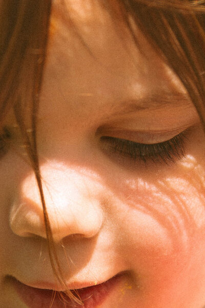 close up of little girls face in sun with her casting shadows on her face