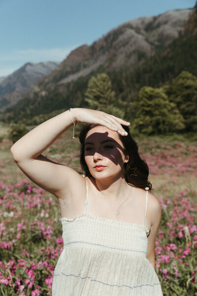 Woman shields her eyes from the sun while surrounded by wildflowers during a portrait photoshoot in the Columbia River Gorge.
