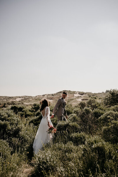 Een bruidspaar kijkt naar elkaar, terwijl ze over de heide lopen.