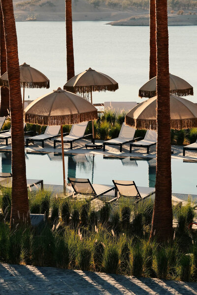 Peaceful poolside scene with sun loungers and natural shades in a verdant, earthy setting. Tailored Oasis Travel Co.