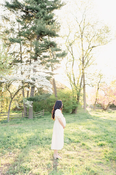 Whimsical spring maternity photoshoot in a field with a mother wearing a white dress.