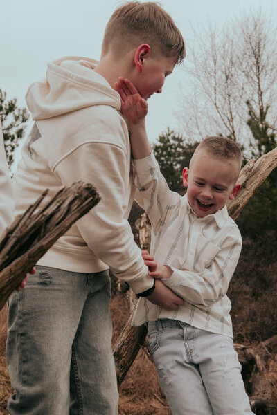 Twee jongens spelen samen in het bos, omringd door bomen en natuur, met blije gezichten en actieve houdingen.