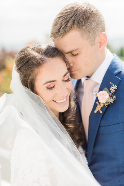 Bride and groom snuggled close together both looking down.