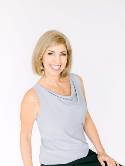 Lora Ulrich in a grey sleeveless top holding a mug, smiling at the camera.
