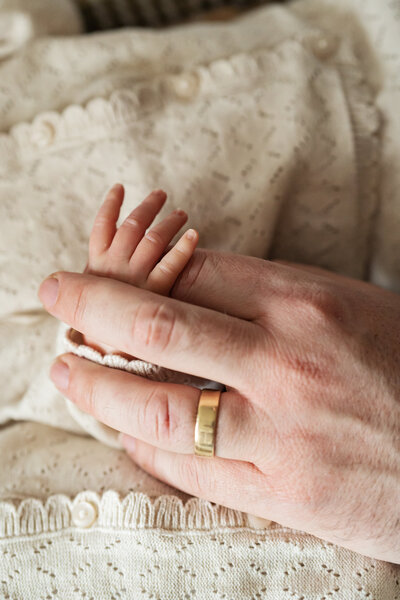 A father's hand holds his baby daughter's illustrating the size difference between his and that of his newborn.