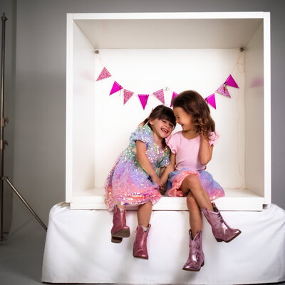 two young girls giggle inside of the white box set at the pittsburgh portrait studio for there famiy photo shoot.
