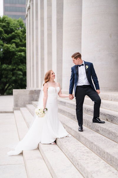 A groom in a blue tux leads his wife up the stairs of the Ohio Statehouse