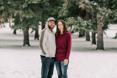 Husband stands behind wife with his arms around her.