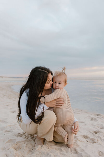 Mother bending down and kissing toddler on cheek on a beach