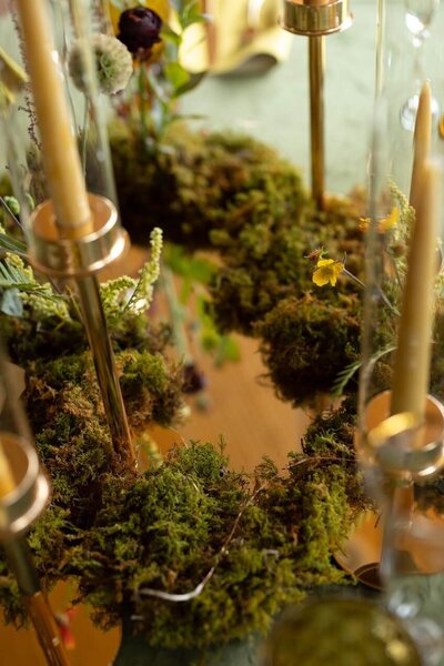 A closeup of a wedding centerpiece with moss and wax candles in glass candelabras