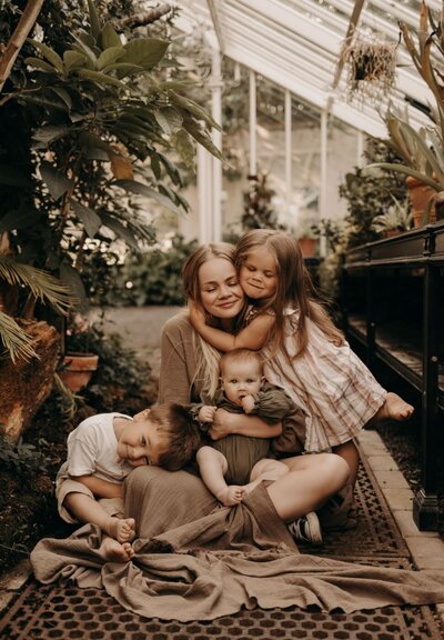 Mother embracing her three young children in a greenhouse setting during a Mullingar family shoot