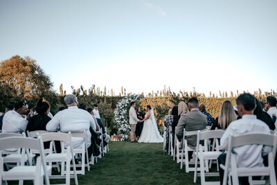 Couple exchanging vows at outdoor wedding ceremony in New Zealand with guests seated, photographed by Zanthe Vorsatz.