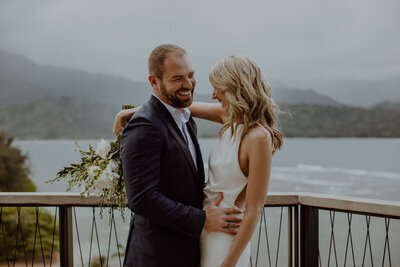 Bride and groom snuggle on balcony overlooking the Hanalei Bay
