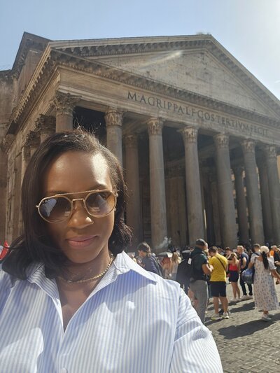 Nadia Forte exploring the historic Pantheon in Rome, Italy, wearing sunglasses and a striped shirt, surrounded by fellow travelers.