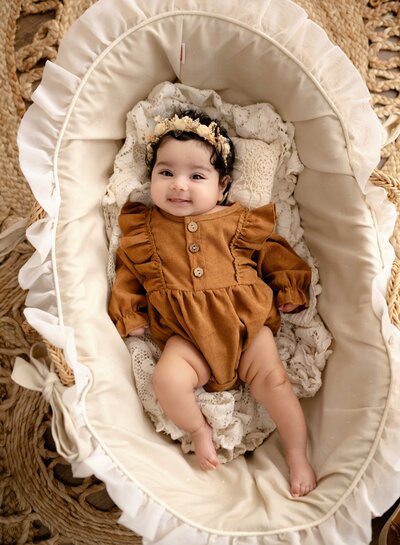 baby girl laying down in a moses basket and smiling at the camera. Milestone baby photo taken at Atlanta Maternity photo studio in Woodstock GA.