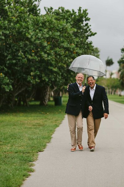 Two Men walking under Umbrella at their Destination Elopement